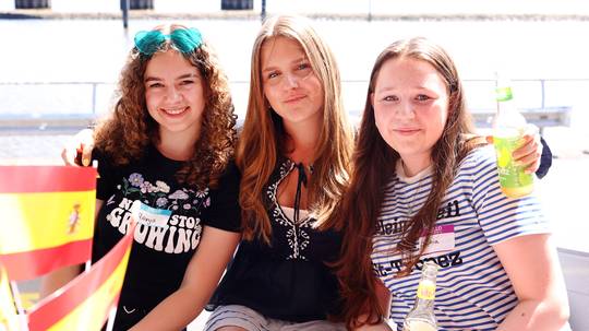 Foto mit drei Zugvogel-Stipendiatinnen, die draußen vor der Stiftung sitzen und spanische Flaggen vor sich haben