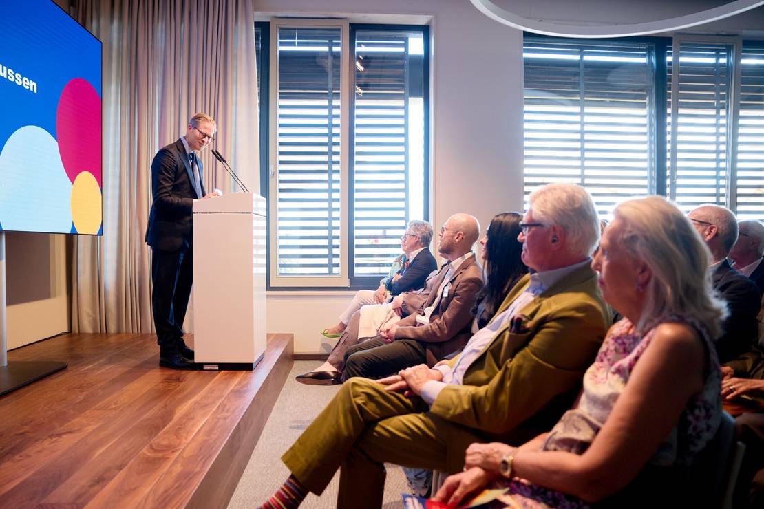 Foto: Ein Mann steht auf einer Bühen und hält eine Rede, rechts ist das Publikum zu sehen.