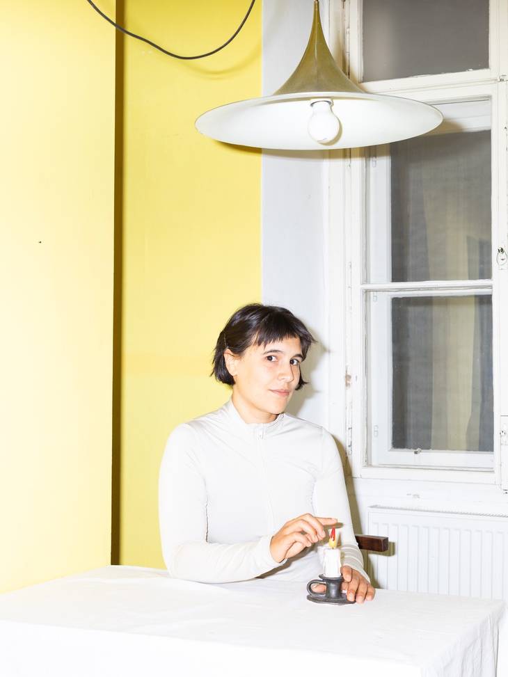Foto von Sophie Allerdinger. Sie sitzt am Tisch und hält den Finger in eine Kerze.