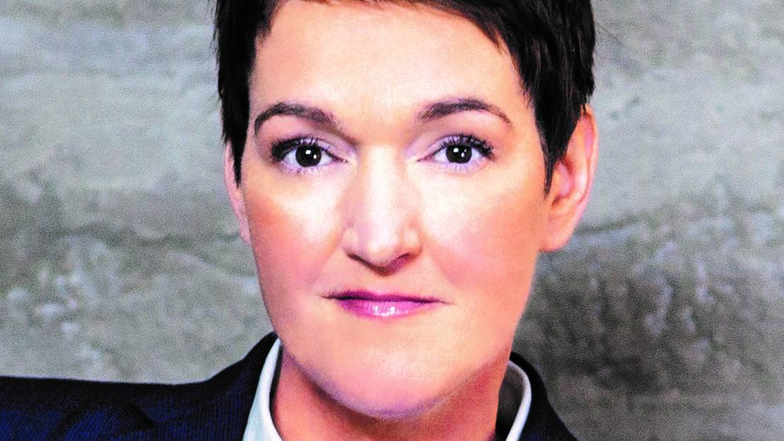 Eine Frau mit kurzen, schwarzen Haaren, die freundlich in die Kamera schaut. Sie trägt ein weißes Hemd und einen dunklen Blazer.