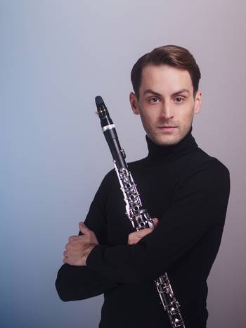 Porträt des Klarinettisten Roman Gerber vor blauem Hintergrund, in der Hand seine Klarinette